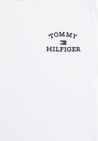 T-shirt en coton blanc avec le texte brodé en noir "TOMMY HILFIGER" et un petit symbole de logo coloré, texture lisse et design à col ras du cou.