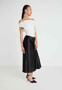 Vit off-shoulder topp med svarta prickar, matchad med en svart satin midi kjol. Svarta spetsiga klackskor fulländar outfiten.