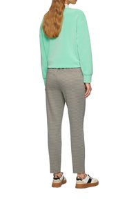 Miętowy sweter z prążkowanymi mankietami, w zestawieniu z wzorzystymi szarymi spodniami. Model nosi białe i czarne sneakersy z brązową podeszwą.