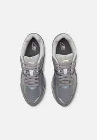 Chaussures de sport grises avec une tige en mesh et en daim, bout arrondi, col rembourré et laçage à l'avant. Logo "N" notable sur le côté.