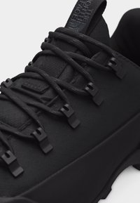 Κοντινό πλάνο μαύρου ορειβατικού παπουτσιού με υφασμάτινη υφή, στρογγυλά κορδόνια περασμένα από μαύρους γάντζους κορδονιών και παχιά ελαστική σόλα.