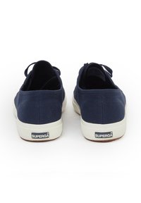 Sneakers in tela navy con design low-profile, caratterizzati da una suola in gomma bianca e un accento del tallone con marchio. La vista posteriore mostra una superficie morbida e un dettaglio a loop.