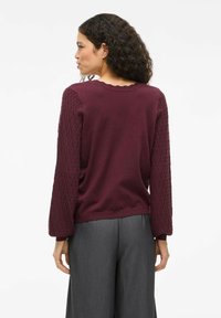 Pull marron avec des manches texturées en tricot et un col en dentelle, associé à un pantalon large gris.