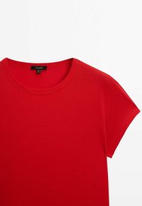 T-shirt rouge à manches courtes avec col rond, en tissu lisse, et une étiquette noire à l'intérieur au niveau de la nuque.