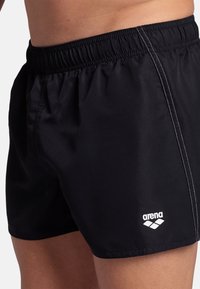 Černé plavky s hladkým povrchem, elastickým pasem, bílým kontrastním stehem a malým bílým logem "arena" na spodní přední části.