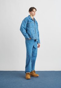 Casaco de ganga azul e calças soltas combinando. Botas castanhas com atacadores. Tecido leve com detalhes clássicos de botões e uma silhueta descontraída.