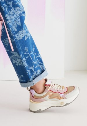La sneaker presenta una toma in rete beige con accenti rosa e viola pastello, una suola spessa bianca e un dettaglio metallico dorato sul tallone.
