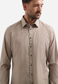 Langarmshirt in beige met een geometrisch patroon. Het heeft een knoopsluiting aan de voorkant, een puntige kraag en een gladde stofstructuur.