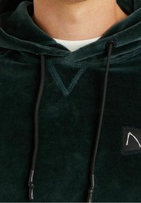 Tmavě zelená fleecová mikina s výstřihem do V, nastavitelnými černými šňůrkami a malou černou nášivkou s bílým logem na hrudi.