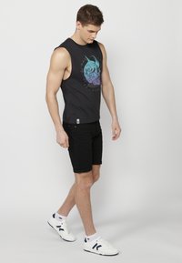 Svart ärmlös tröja med färggrafisk tryck, i kombination med svarta shorts och vita sneakers med marinblå detaljer. Slim fit design.