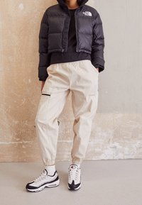 Svart kort puffjacka med dragkedja, krämfärgade cargobyxor med elastiska muddar och fickor, svart-vita sneakers med mesh-accenter.