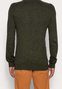 Pull vert avec une texture côtelée, orné de taches dispersées d'orange et de bleu. Manches longues et encolure arrondie.