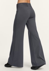 Graue weit geschnittene Hose mit einem gerafften Bund, aus glattem Material, mit einem entspannten Sitz und dezenten Nahtdetails, kombiniert mit schwarzen Schuhen.