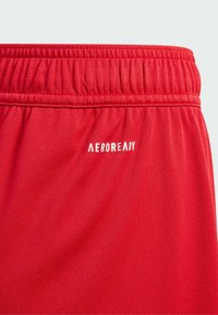 Rode sportshorts met een elastische tailleband, gemaakt van een gladde, vochtafvoerende stof. "AEROREADY" logo in het wit aan de linkerkant.