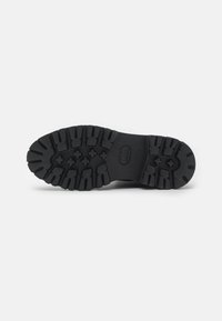 Semelle de chaussure en caoutchouc noir avec un motif de texture et des rainures profondes pour une meilleure adhérence, ainsi qu'une zone centrale lisse pour plus de stabilité.