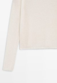 Jasna kremowa sweter z dzianiny z długimi rękawami, luźnym krojem i lekko skróconym dołem. Miękka tekstura z delikatnymi detalami.