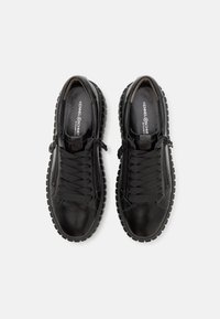 Paire de baskets noires en cuir à lacets avec semelles épaisses crantées et fermetures éclair latérales, vues de dessus sur fond blanc.