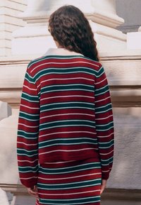 Pull rayé rouge, vert et blanc avec une coupe décontractée, des manches longues et un ourlet côtelé. Le dos présente un motif tricoté simple et texturé.