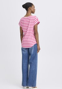 Rohelise ja valge triibuline lühikeste varrukatega T-särk, ümara kaelusega ja lõdva istuvusega, koos laia säärega siniste teksapükstega.