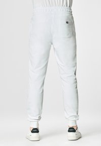 Pantaloni della tuta bianchi con vita elasticizzata e polsini. Presentano una sola tasca posteriore con un piccolo etichetta del logo. Tessuto liscio e design aderente.