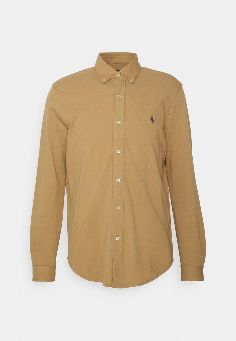 Camisa de manga larga con botones en algodón color beige, presenta un cuello estándar, cierre frontal con botones y un pequeño logo bordado en el pecho.