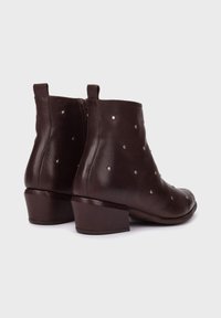Bruine leren enkellaarzen met lage blokhakken, versierd met zilveren studs. Voorzien van een ritssluitingen en een gladde textuur op het oppervlak.