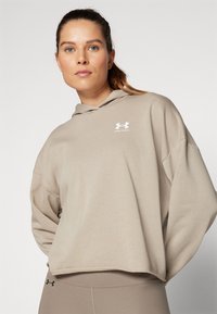 Sudadera con capucha beige de corte holgado, con un logo blanco de Under Armour. Tejido suave con un diseño casual y costuras de hombros caídas.