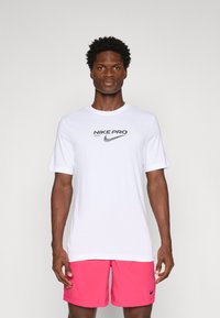 White Nike Pro T-shirt with short sleeves and black logo on the chest, paired with pink athletic shorts featuring a small black logo.