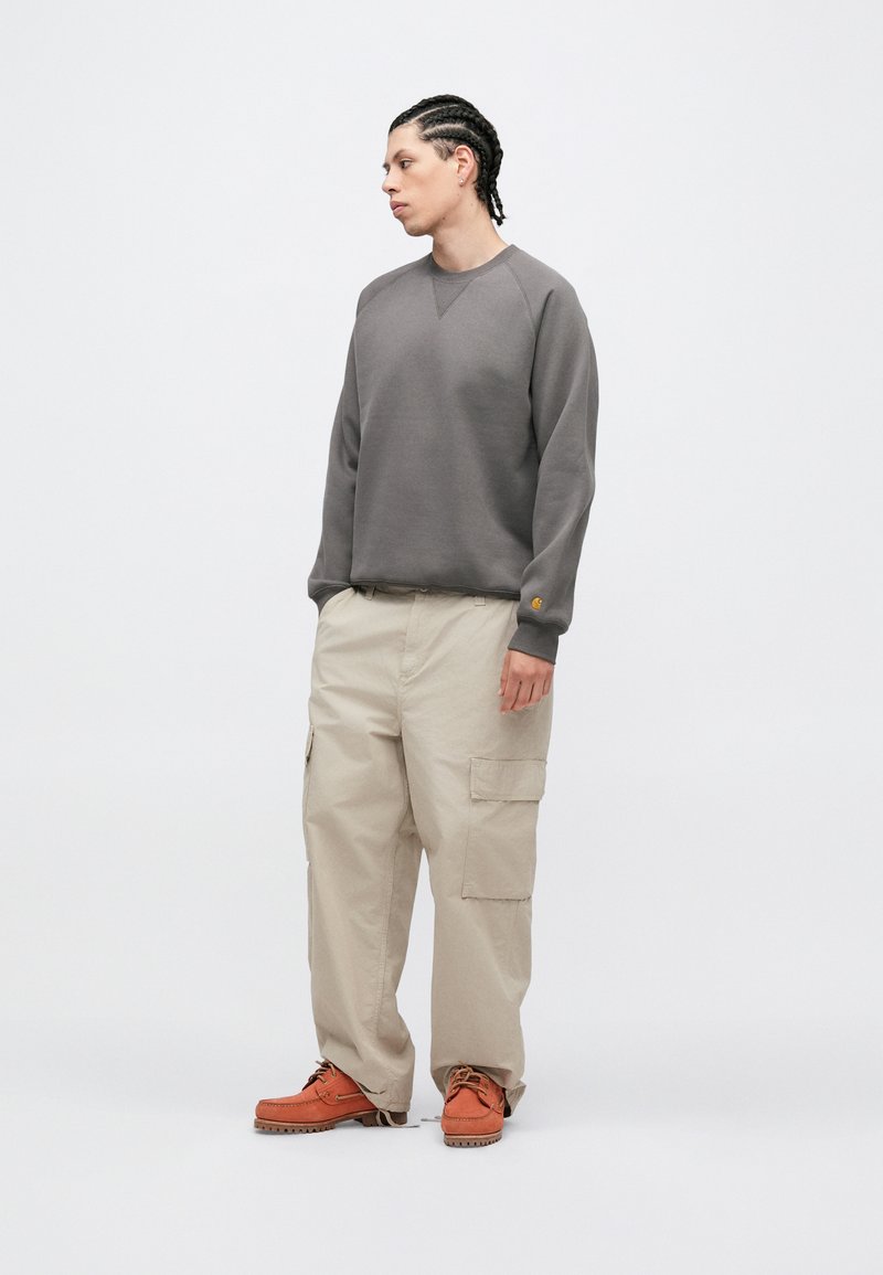 Grå sweatshirt med ribstrikkede manchetter, beige cargobukser med sidelommer og orange sko. Enkel, afslappet pasform og glatte stofteksturer.