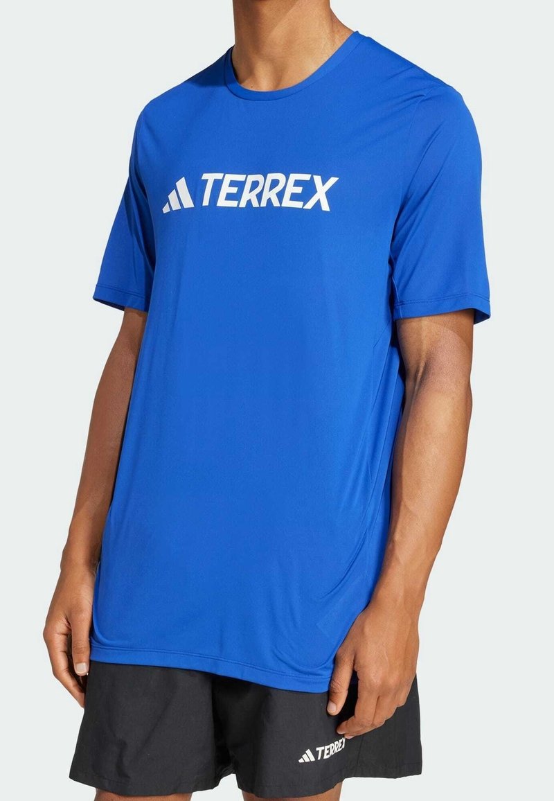Maglietta sportiva a maniche corte blu in materiale traspirante; presenta un logo bianco "TERREX" sul petto. Vestibilità ampia e texture liscia.