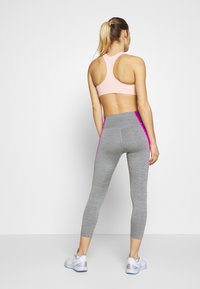 Lys pink sportsbh med racerback-design, parret med højtaljede grå leggings med rosa sideakster og en tætsiddende pasform.