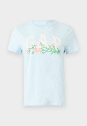 Maglietta a maniche corte azzurro chiaro con grandi lettere bianche "GAP" e un motivo floreale orizzontale in rosa e verde sul petto.