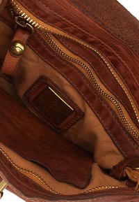 Interno di borsa in pelle marrone con fodera in tessuto, dotata di molteplici tasche con cerniera e una targhetta in metallo dorato per l'identificazione del marchio.