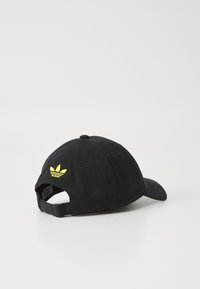 Svart bomullsbasketcaps med et gult brodert logo på baksiden, justerbar stropp og buet skjerm. Teksturen er glatt.