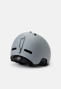 Pelēks ķivere ar matētu virsmu, ventilācijas atverēm, regulējamu siksnu un logo detaļām. Iespējo aizmugurējo skavu, lai nodrošinātu drošu piegulšanu.