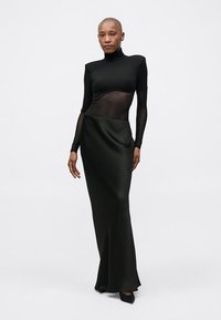 Black long-sleeve gown with a fitted bodice featuring sheer panels and a flowing satin skirt. Smooth texture, minimal design, and monochromatic color.