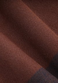 Brązowa filcowa tkanina o gładkiej teksturze, charakteryzująca się ciepłym, bogatym kolorem i delikatnymi odcieniami, tworzącymi warstwowy efekt.