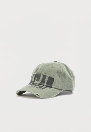 Iznosena zelena bejzbolska kapa s crnim izblijedjelim natpisom i malim rupama na obodu, na bijeloj pozadini.