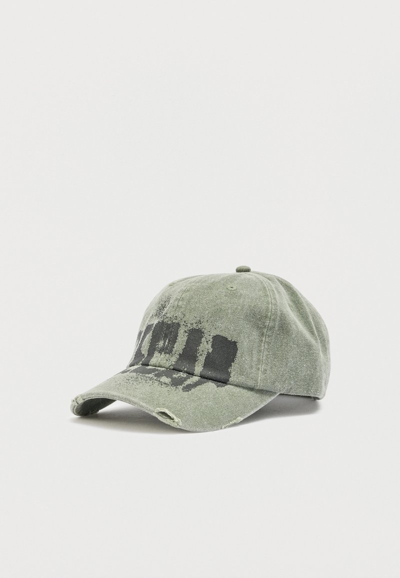 Φθαρμένο πράσινο καπέλο μπέιζμπολ με μαύρο φθαρμένο σχέδιο μπογιάς και μικρές τρύπες στο γείσο, σε λευκό φόντο.