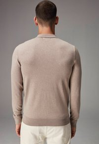 Pulover bej cu mânecă lungă, cu tiv și guler ribflat, fabricat dintr-un material moale, având o textură netedă și un design ajustat.