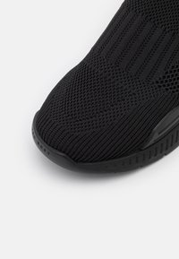 Gros plan sur l'avant d'une sneaker en tissu tricoté noir avec des motifs texturés et une semelle en caoutchouc noire.