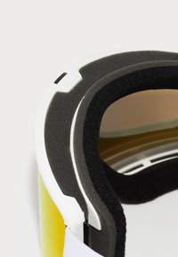 Lunettes de ski avec un intérieur en mousse noire, une monture blanche et une lentille teintée en jaune, dotées d'un bouton sur le côté pour les réglages.