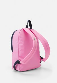 Zaino rosa con spallacci imbottiti, forma piatta e dettagli blu navy. Realizzato in tessuto resistente con un piccolo logo verde.