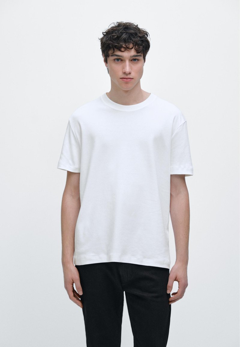 White cotton t-shirt with a crew neckline, short sleeves, and a relaxed fit, paired with black jeans. Simple and minimalistic design.