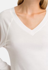 Top a maniche lunghe a scollo a V in morbido tessuto bianco, con maniche raglan e un design aderente e liscio con una leggera lucentezza.