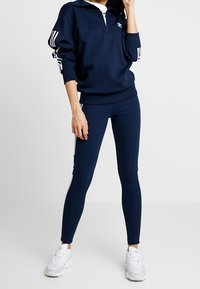 Pull-over marine avec une fermeture à quart de zip et des accents blancs, associé à un legging marine. Comprend trois rayures blanches sur les manches et les leggings.