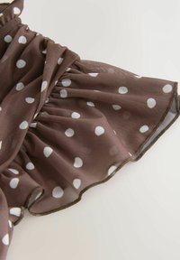 Tessuto marrone a pois con pois bianchi, design arricciato, texture trasparente e orlo volant bordato di rifinitura scura.