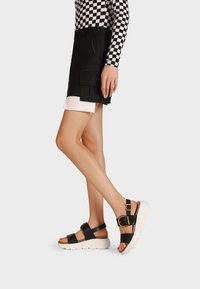 Sandali platform neri con fasce larghe, accentuati da una fibbia dorata e una suola bianca Texturizzata, progettati per comfort e stabilità.