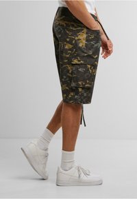 Camo cargo shorts in dark green, gray, and mustard colors; features multiple pockets and an adjustable drawstring at the waistband.