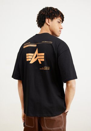 Sort bomulds t-shirt med et stort orange logo på ryggen og tekstdetaljer. Korte ærmer og afslappet pasform. Enkelt foran.